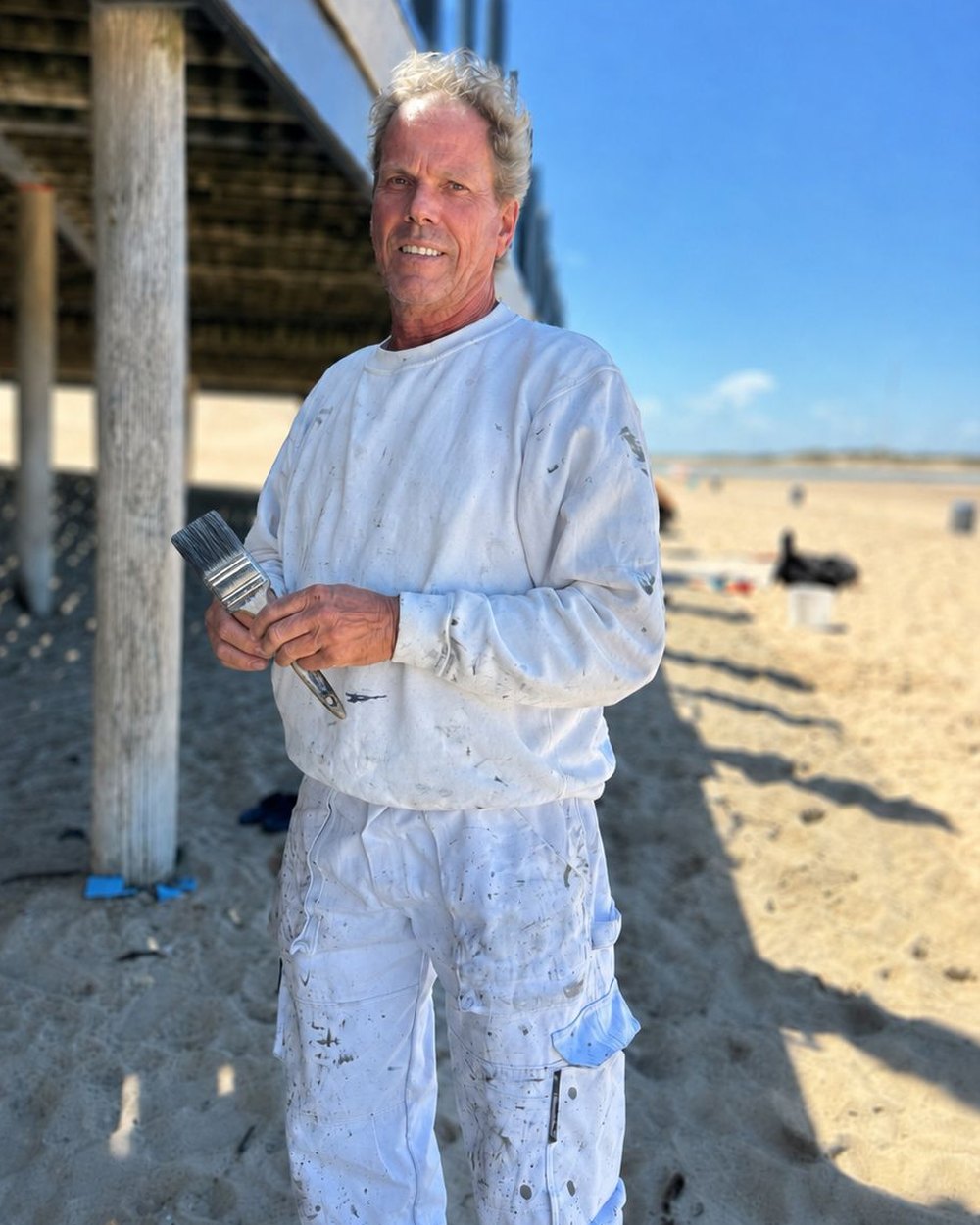 Henk Thiry, onderhoudsschilder uit Oostburg, met kwast aan het werk aan de Zeeuwse kust